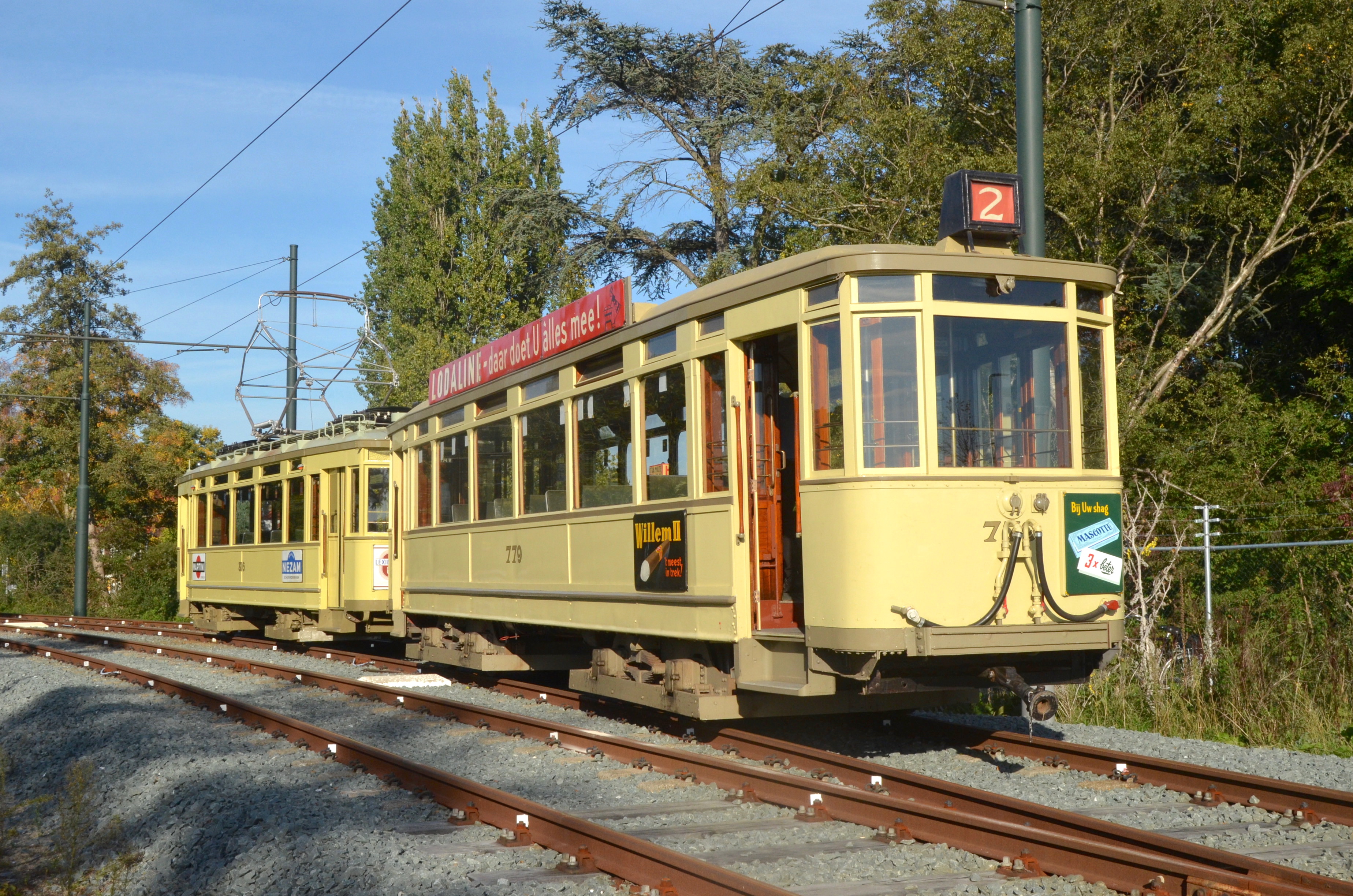 Żółty zabytkowy tramwaj na torach z drzewami w tle