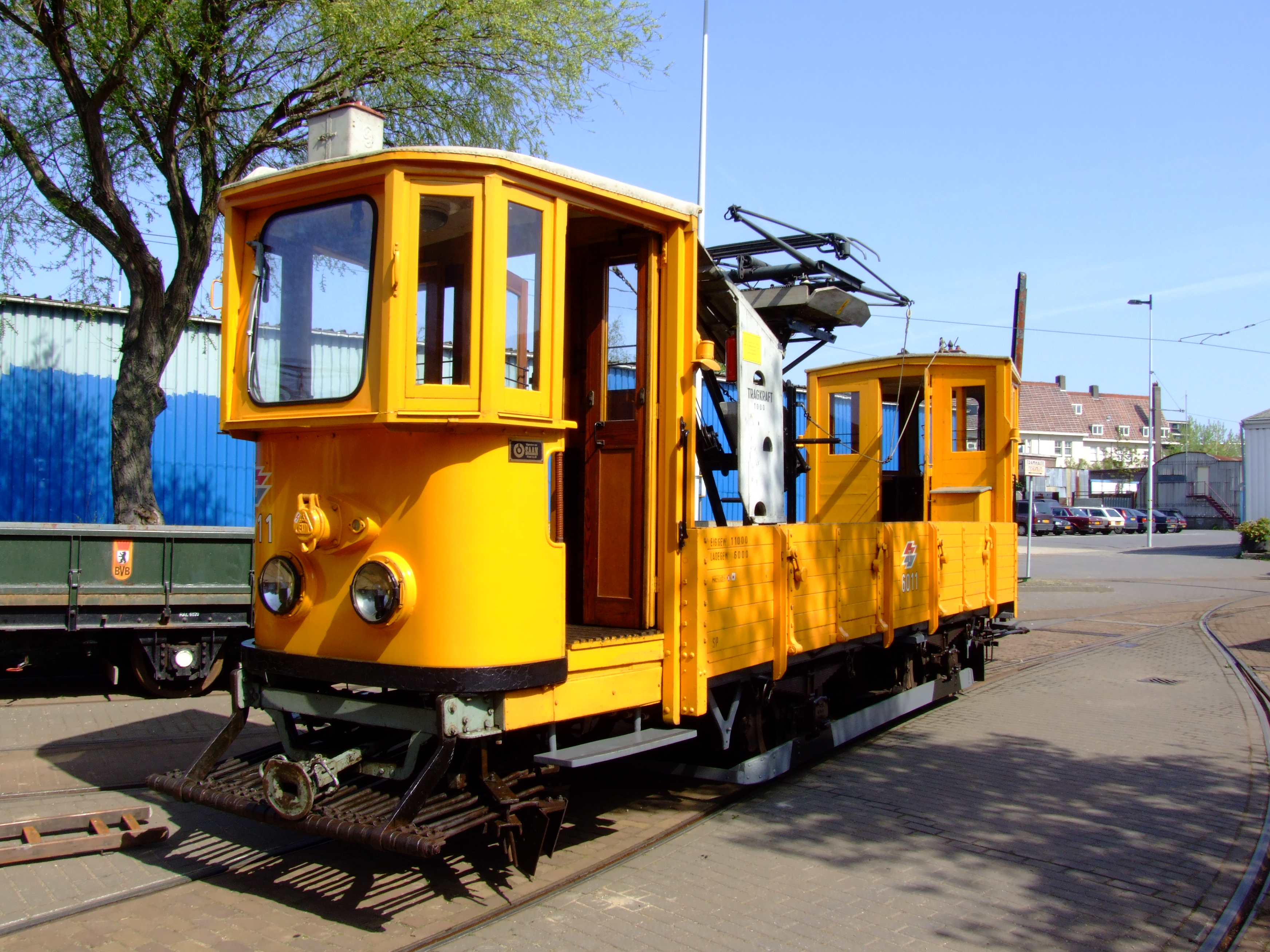 Żółty zabytkowy tramwaj na torach z przewodami napowietrznymi i niebieskim niebem
