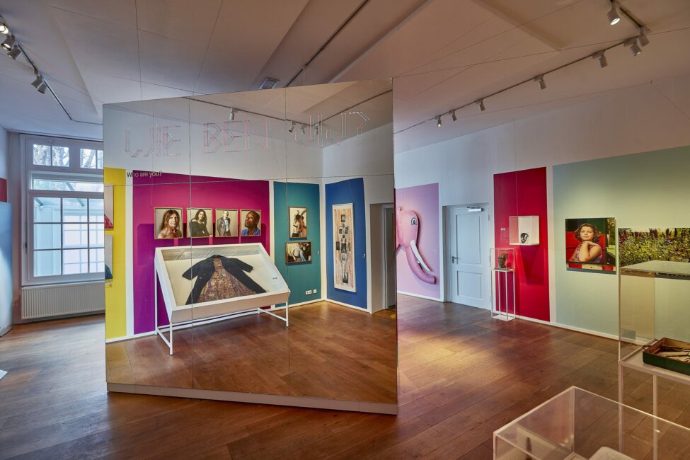 Museum tentoonstellingsruimte met kleurrijke muren waarop diverse kunstwerken en foto's op panelen worden tentoongesteld.