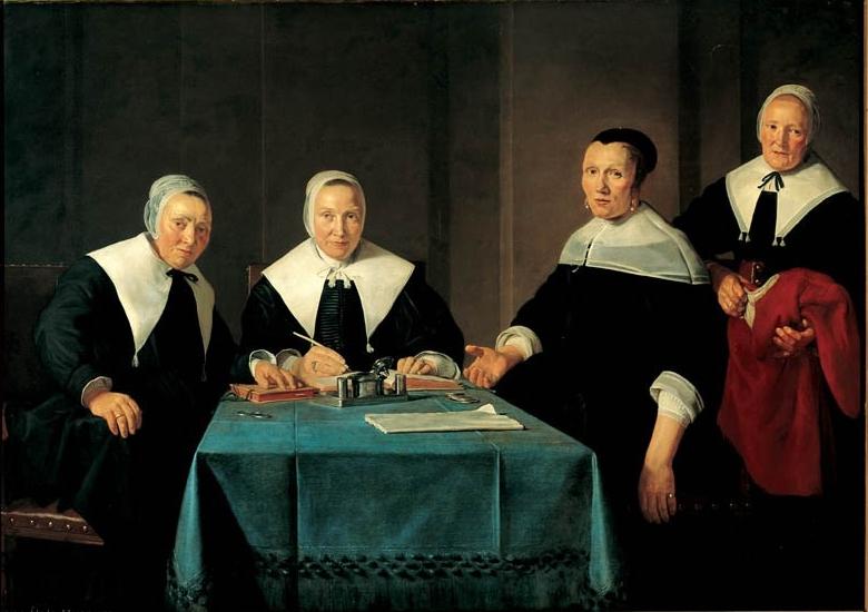Vier figuren in donkere historische kledij met witte kragen, zittend rond een tafel bedekt met een blauwe doek, met boeken en kleine voorwerpen
