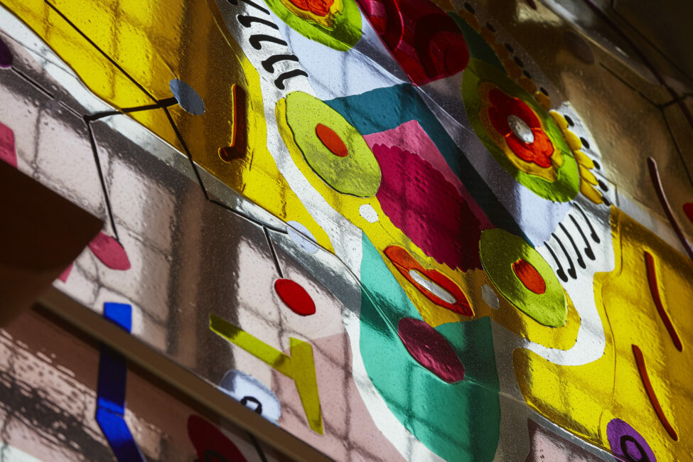 Levendige abstracte plafondkunst met kleurrijke geometrische vormen, cirkelvormige patronen en hangende decoratieve elementen in een museumruimte