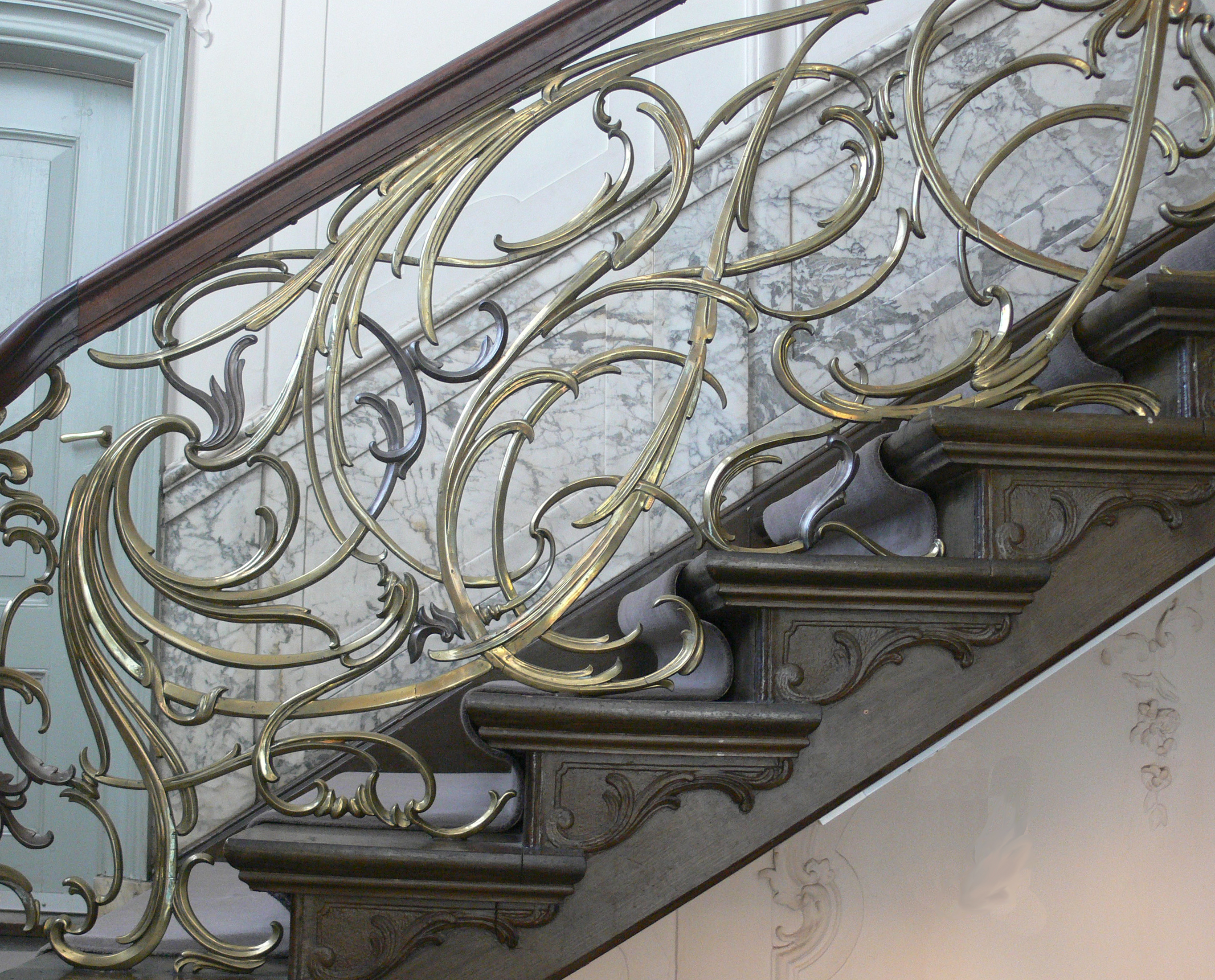 Intricate gold-colored metal railing with scrollwork on a marble staircase inside Museum Van Loon