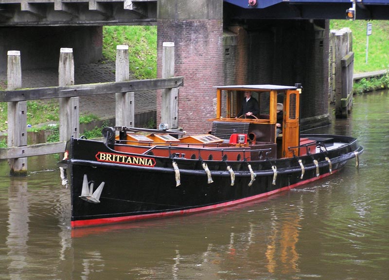 El histórico barco negro y rojo 'Britannia' atracado en un canal bajo un puente de ladrillo en Museumhaven Amsterdam