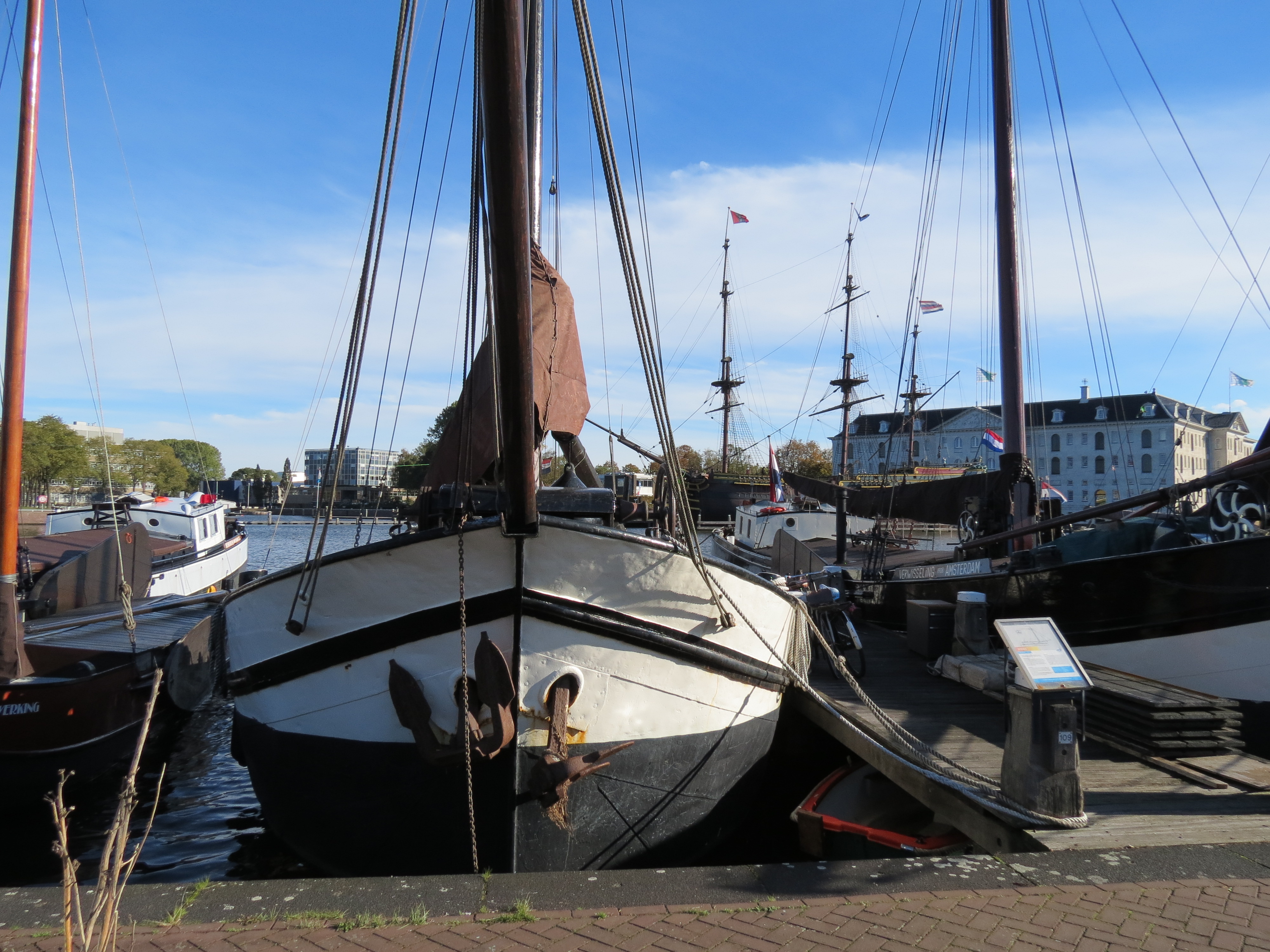 Históricos veleros atracados en el puerto de Museumhaven con cielo azul y edificios de Ámsterdam al fondo