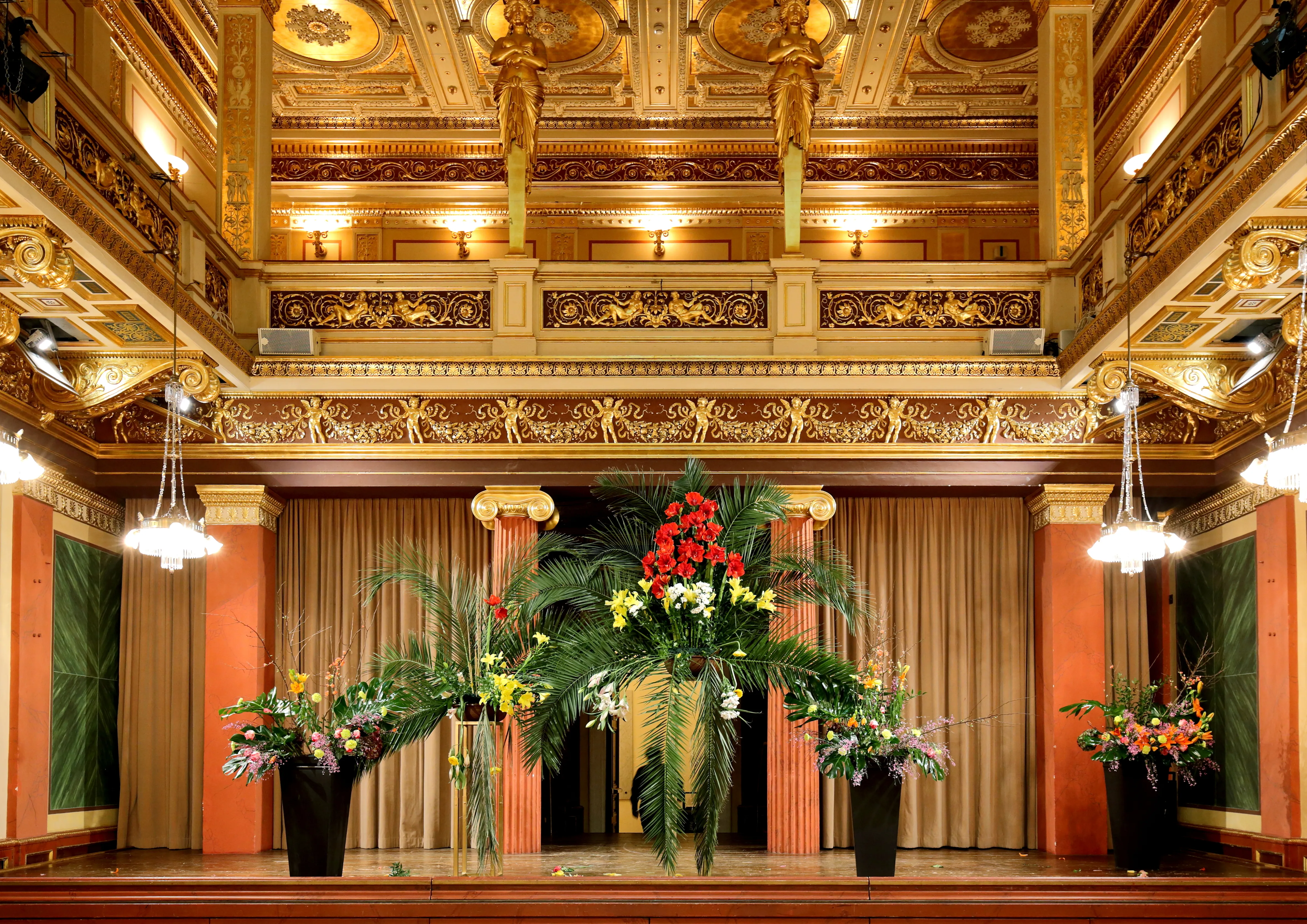Ornamentalne wnętrze Brahms-Saal ze złotymi detalami sufitu, żyrandolami i kwiatowymi aranżacjami na scenie