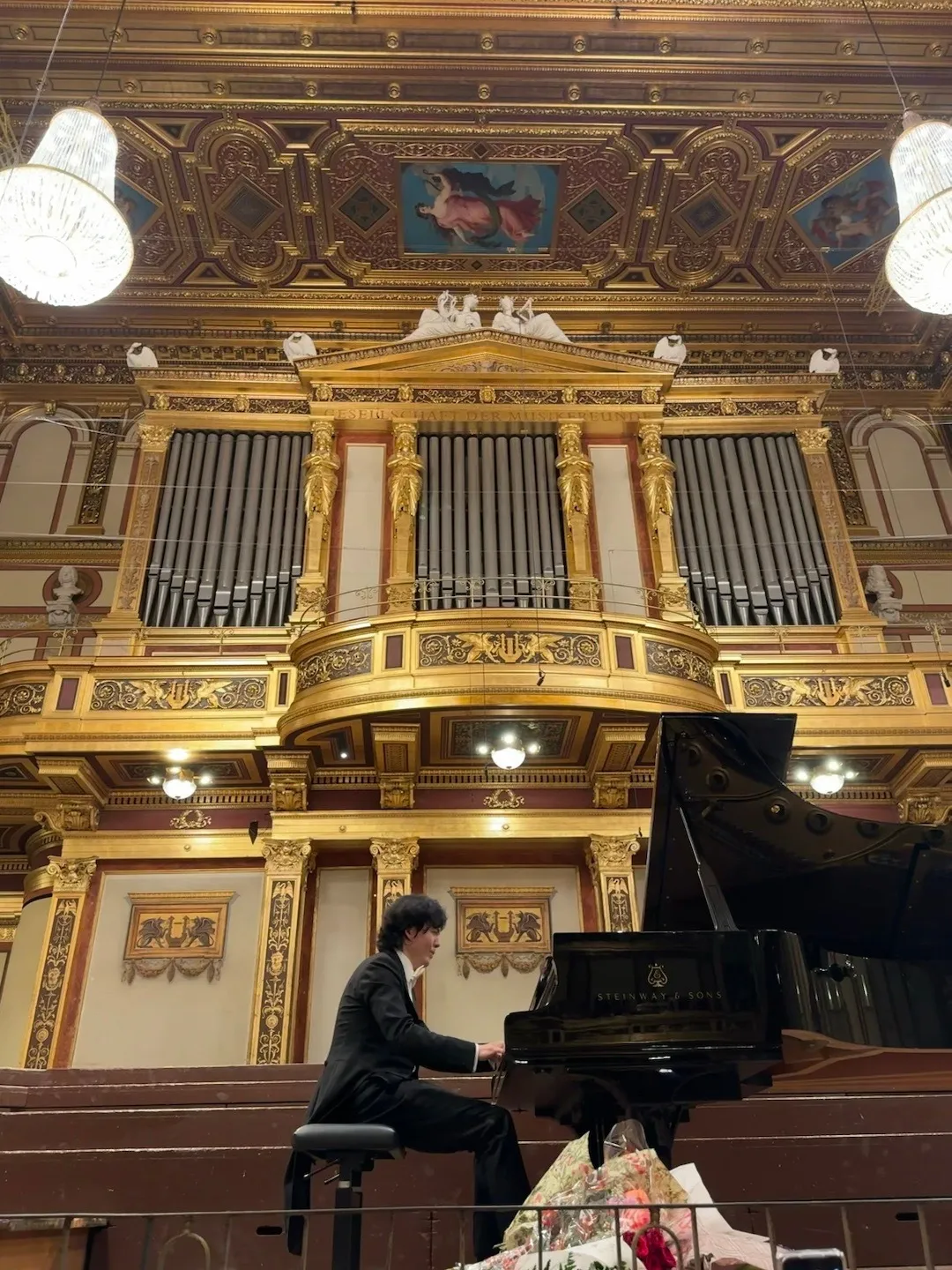 Een pianist die op een vleugel speelt op het podium in de Gouden Zaal van de Musikverein, met een groot gouden orgel en sierlijke plafondversieringen.