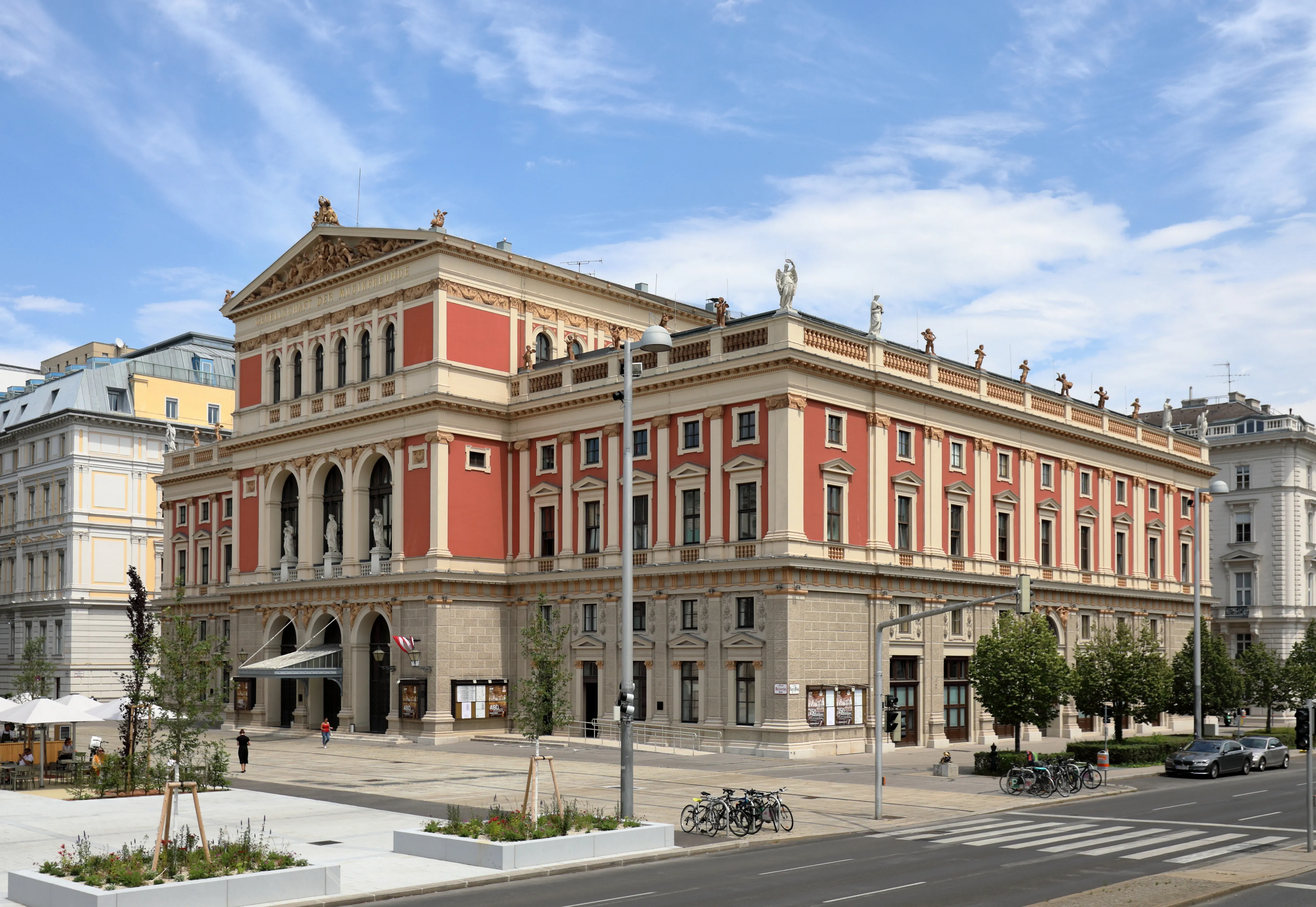 Neoclassicistisch gebouw met een rode en beige gevel, een boogvormige ingang en een sierlijke daklijn onder een blauwe hemel