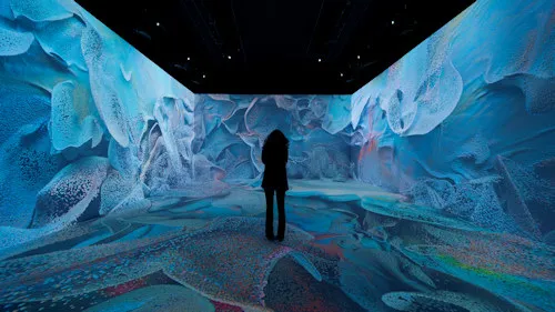 Silhouette of a person standing in a dark room with blue and white abstract projections on the walls and floor