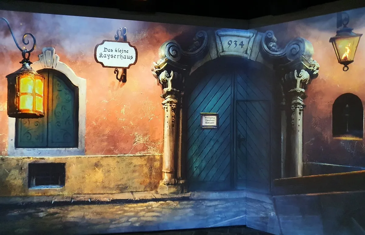 A projected scene of a historic street with a blue door, lanterns, and a sign for 'Das kleine Acherhaus'