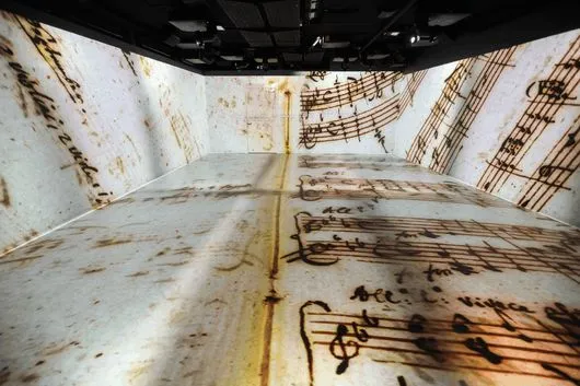 Interior de una exposición inmersiva con partituras musicales proyectadas en paredes y suelo
