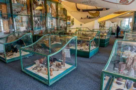 Wnętrze muzeum z gablotami zawierającymi artefakty, wysokim sufitem i modelem łodzi wiszącym od góry