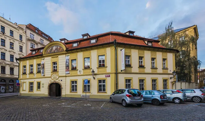 żółty budynek z czerwonym, ceramicznym dachem i łukowym wejściem na brukowanym placu
