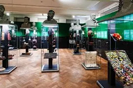 galeria muzealna z przeszklonymi gablotami zawierającymi artefakty, zielonymi podświetlanymi ścianami i drewnianymi podłogami