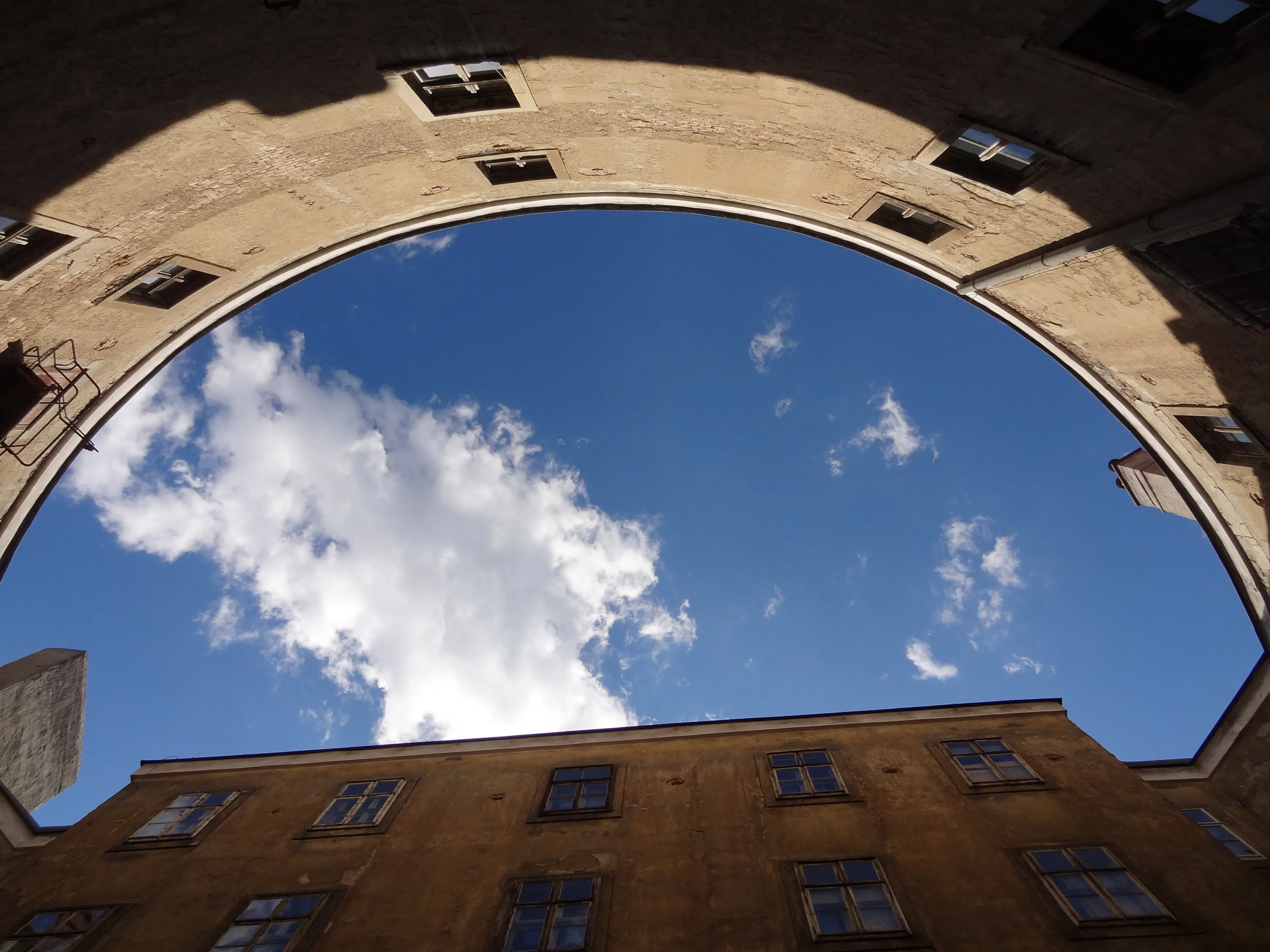 Low-angle view of a large stone archway with a blue sky and clouds visible through the opening