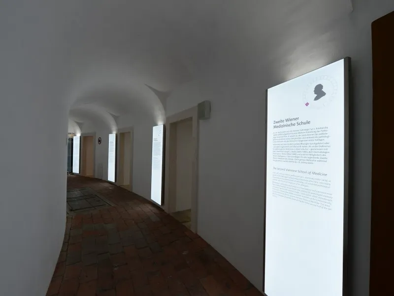 Interior hallway of Narrenturm with arched ceilings, wooden floors, and an illuminated display panel on the wall