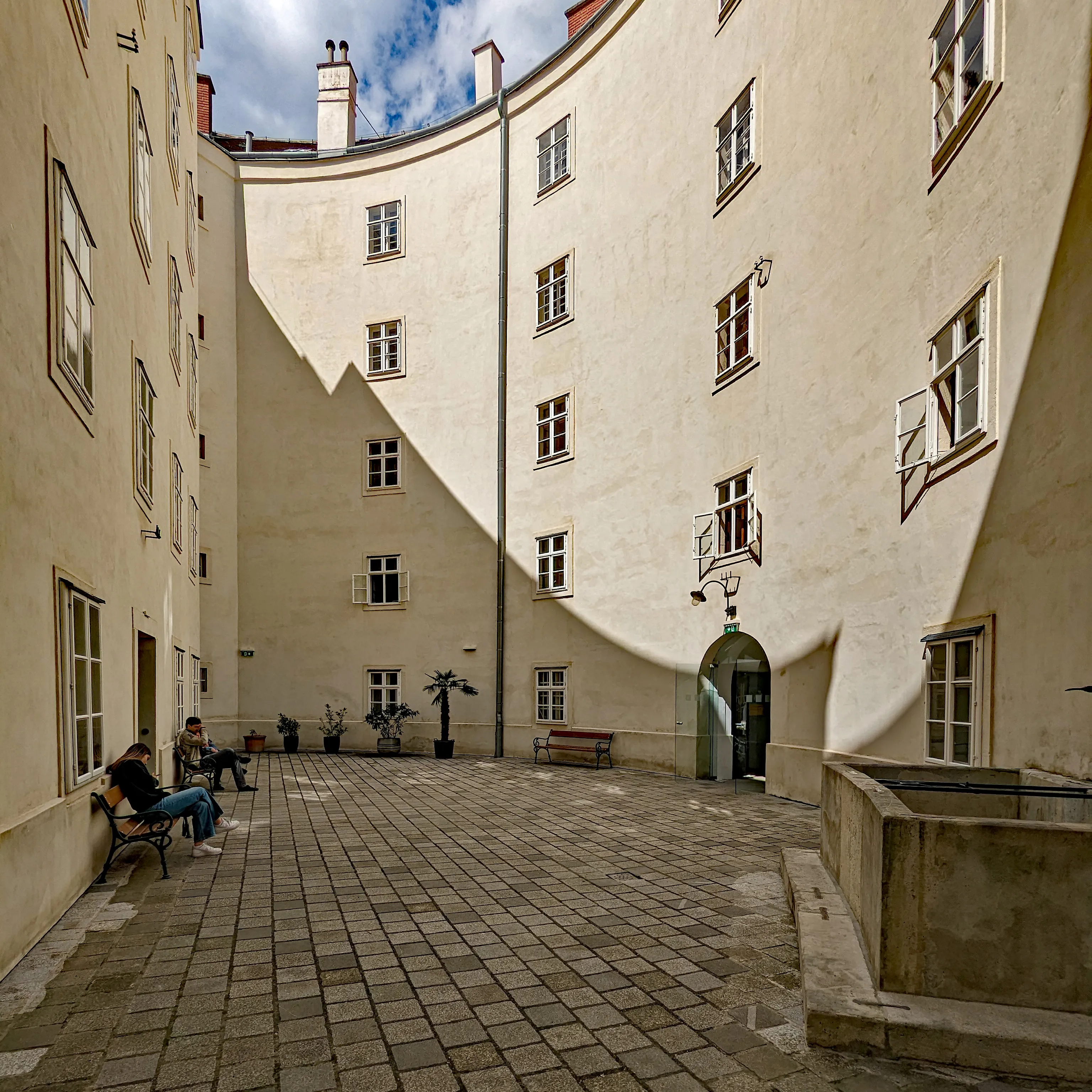 Courtyard of the Narrenturm with cream-colored walls, windows, and people sitting on benches