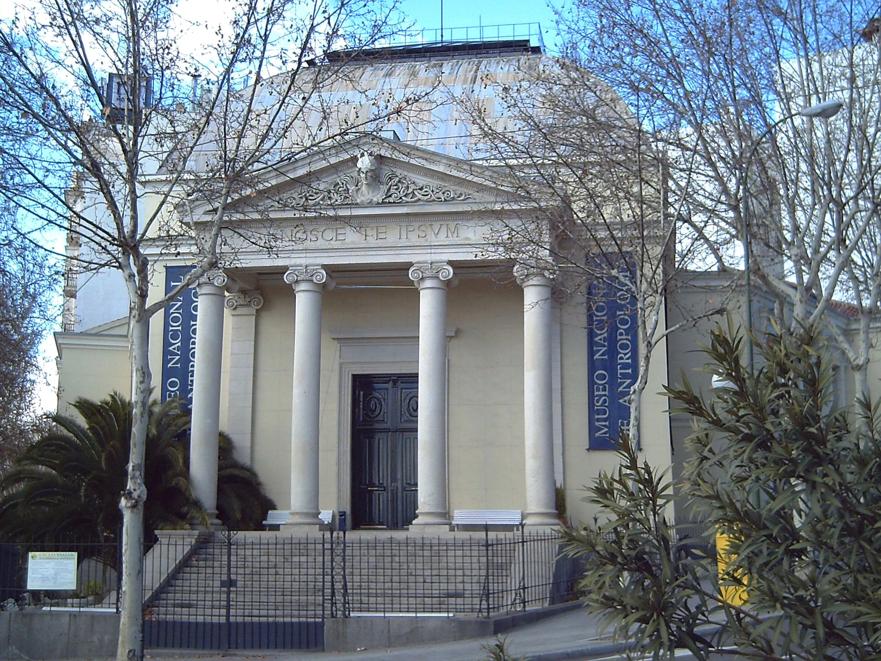 El exterior del Museo Nacional de Antropología con una fachada clásica, columnas y pancartas azules a ambos lados de la entrada.