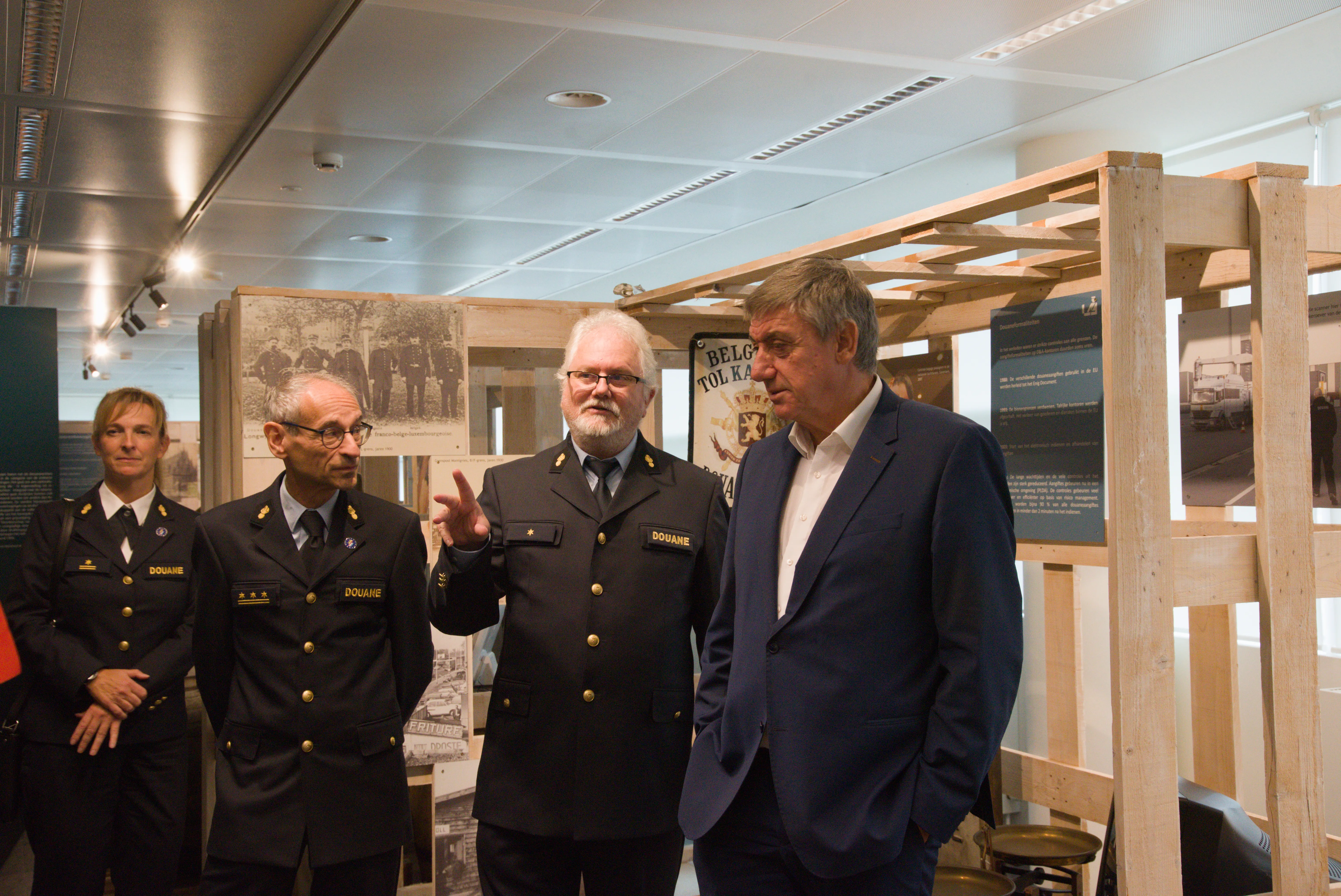 Grupa ludzi, w tym funkcjonariusze U.S. Customs w ciemnych mundurach, stojąca wewnątrz muzeum na tle paneli wystawowych i drewnianej konstrukcji szkieletowej.