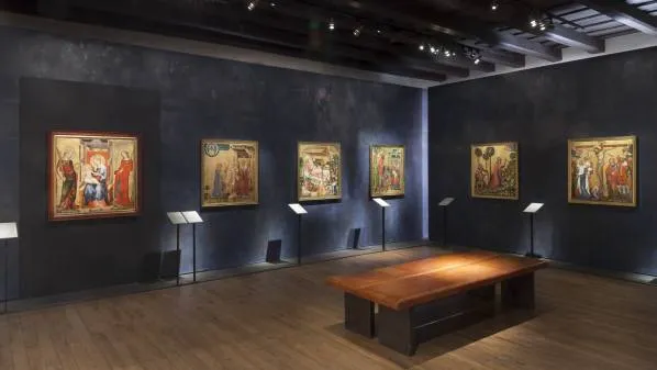 Galerij met middeleeuwse schilderijen aan donkere muren en een houten tafel