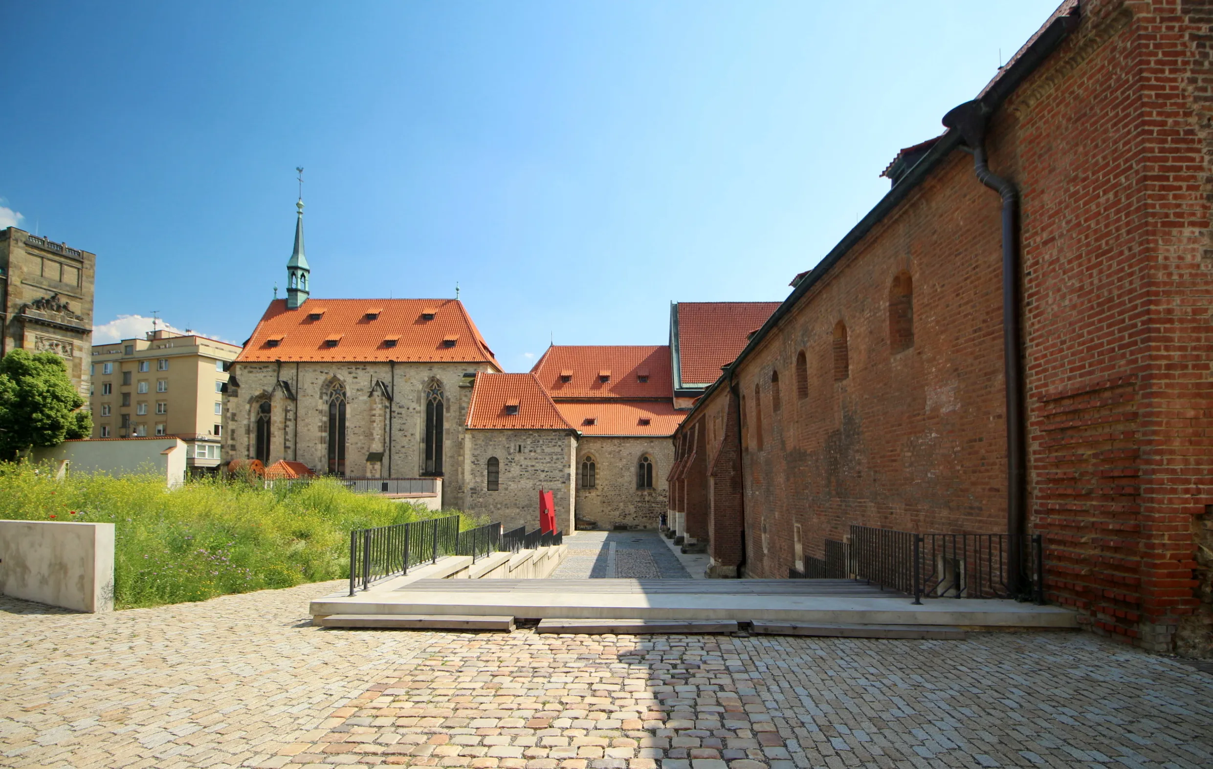 Een binnenplaatsuitzicht op het Agnesklooster van Bohemen met rood pannendaken, bakstenen muren en een kerktoren onder een blauwe hemel