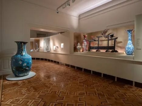 Binnengalerij met houten vloer, witte muren en vitrines met vazen en artefacten