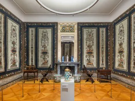 Ornate galerijkamer met wandtapijten, een centrale vitrine en een houten vloer