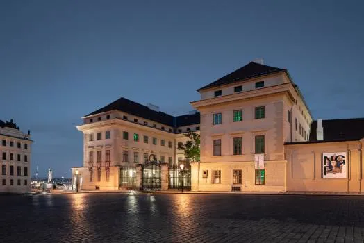 Neoclassic paleisgebouw bij schemering met verlichte ramen en een geplaveid plein ervoor
