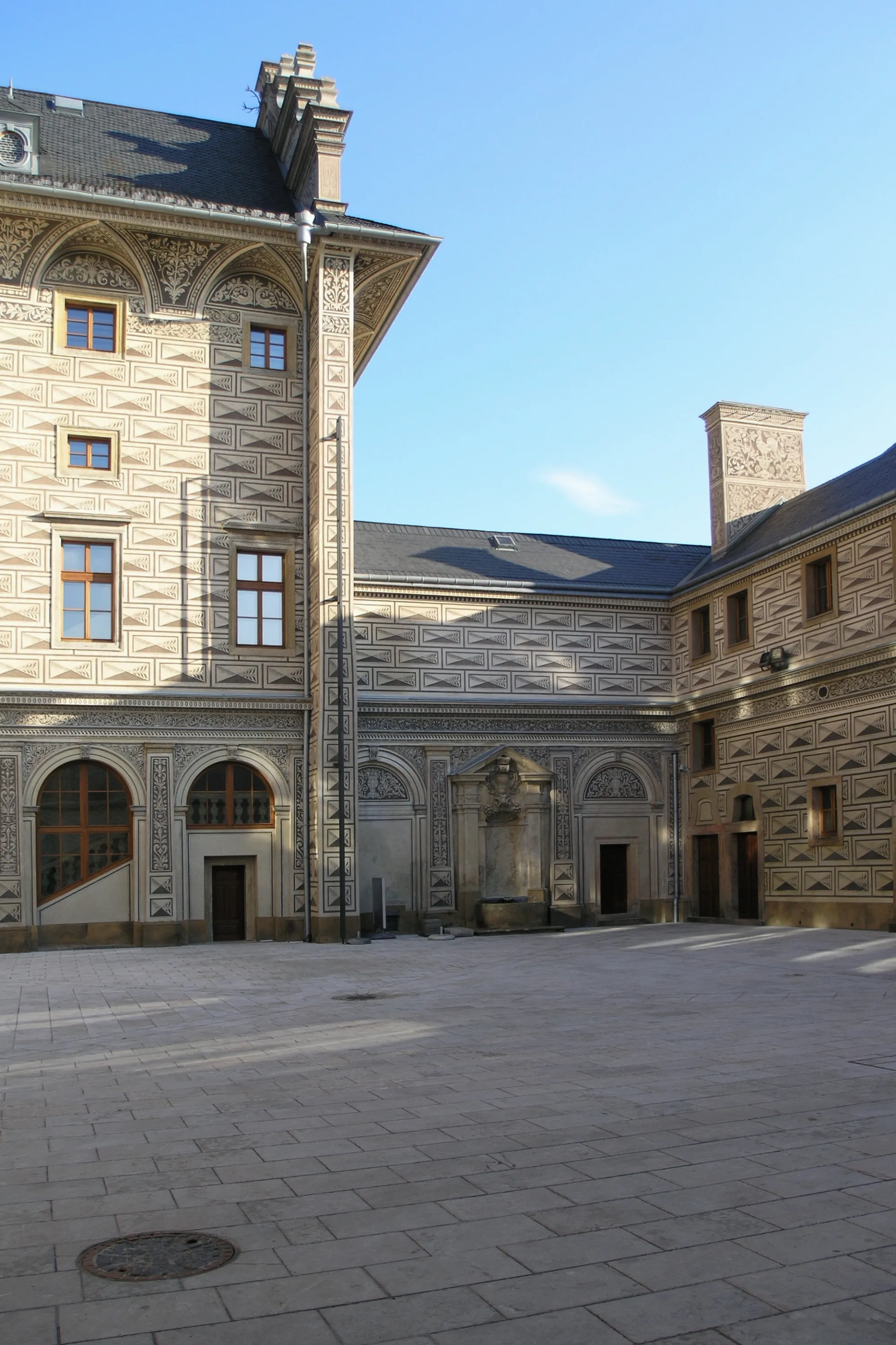 Dziedziniec Pałacu Schwarzenberg z ozdobnym kamieniarstwem i łukowymi drzwiami pod czystym, błękitnym niebem