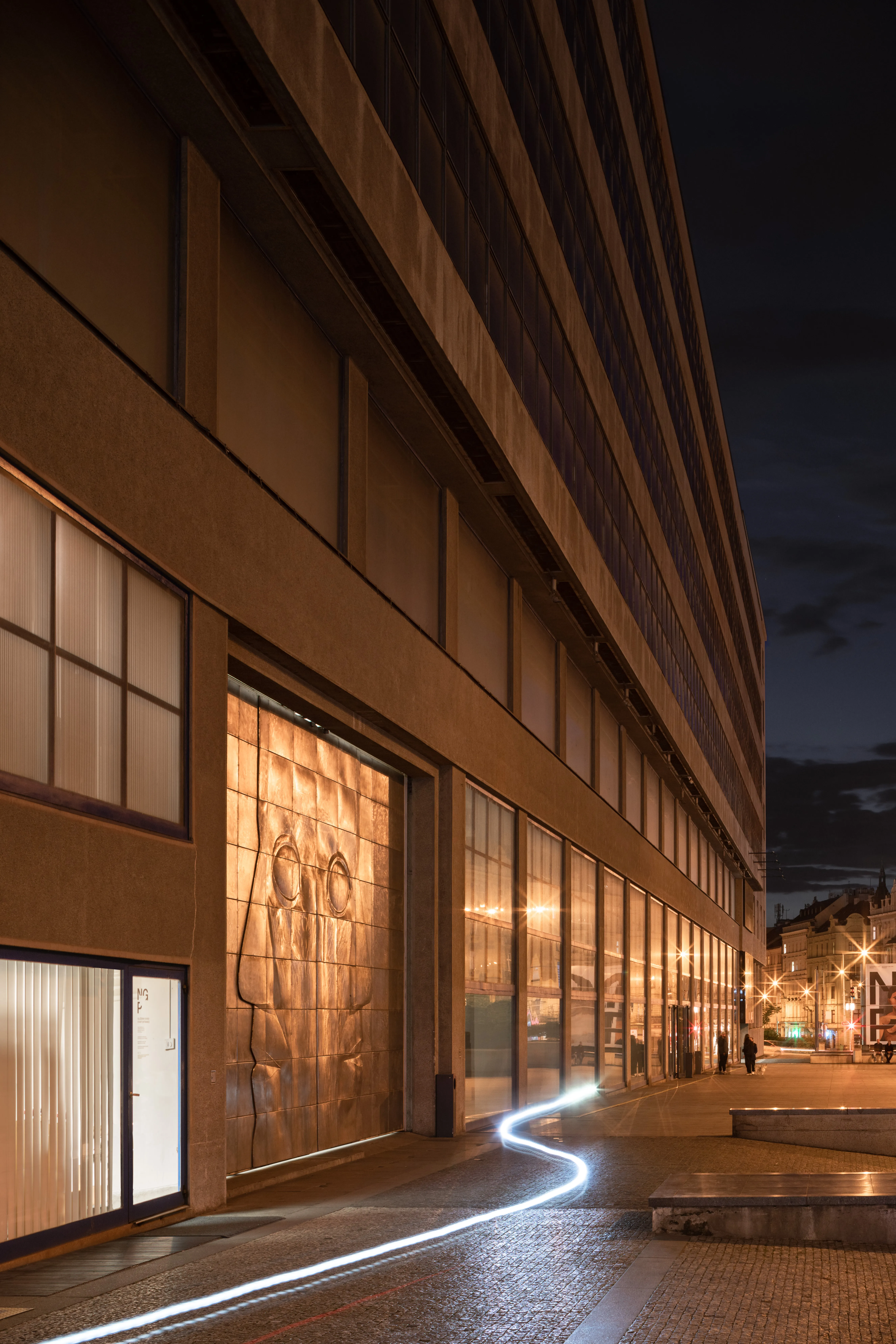 exterior de edificio moderno por la noche con ventanas iluminadas y una escultura de relieve de bronce