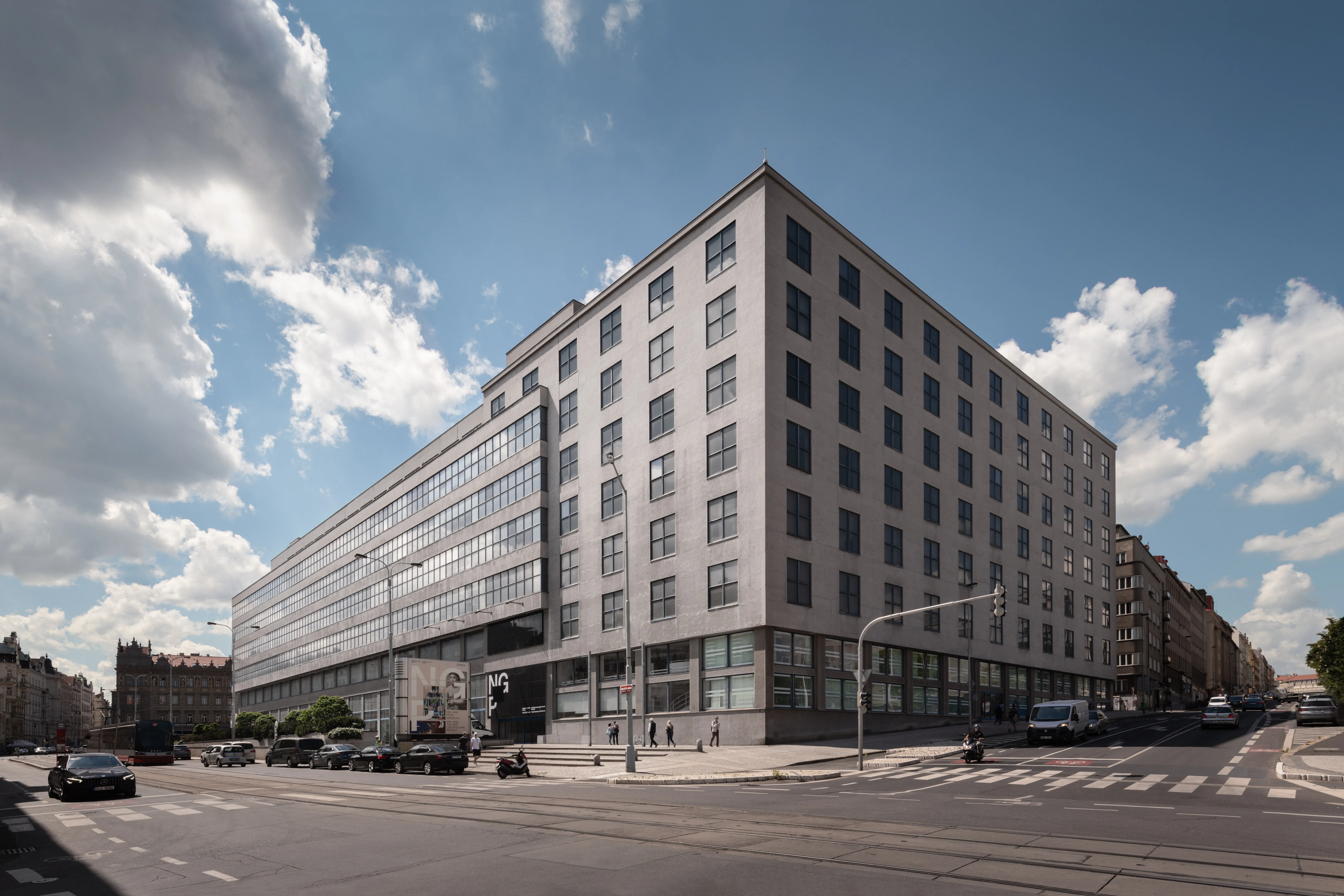 Edificio modernista con fachada gris y grandes ventanales bajo un cielo azul con nubes