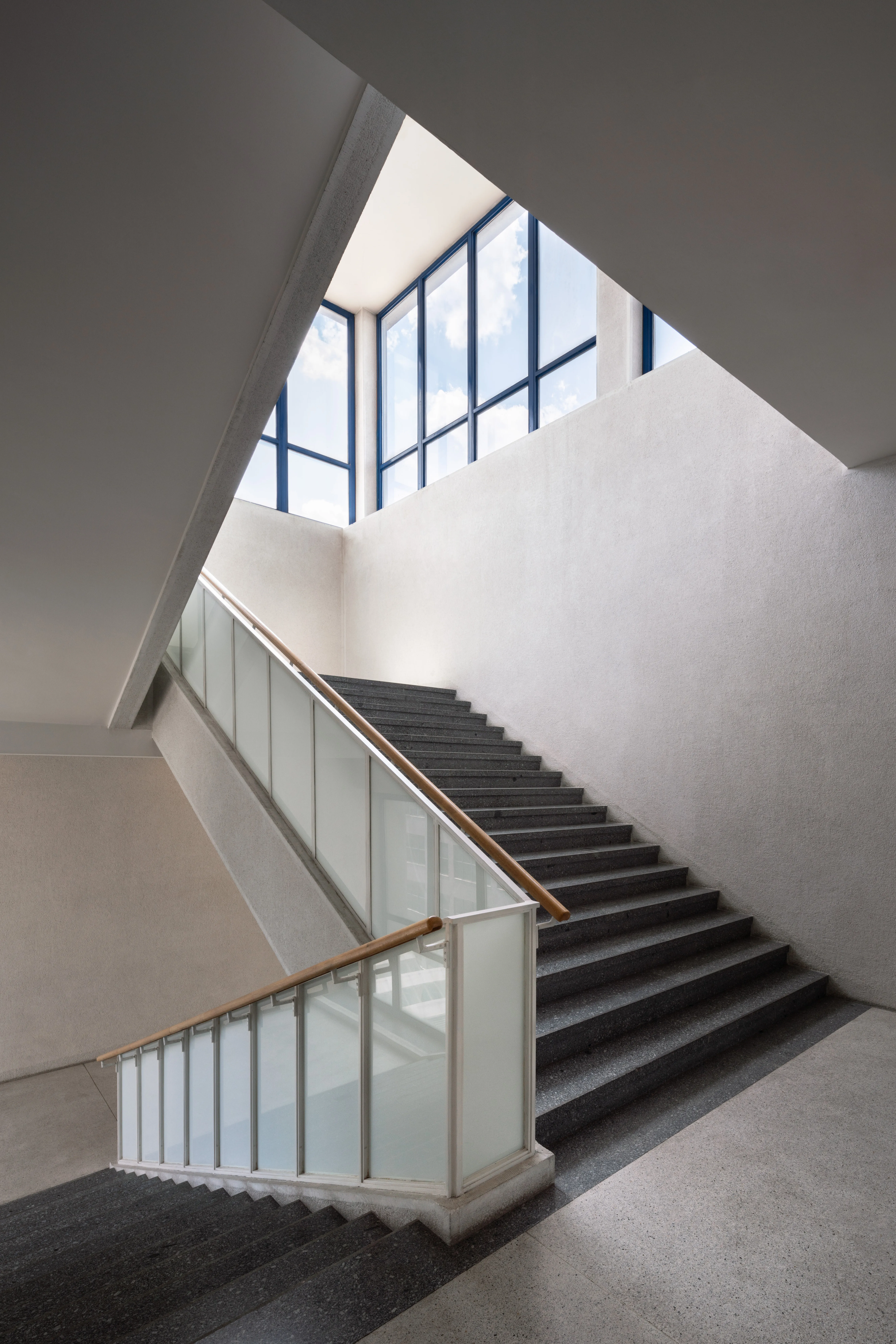 Modern staircase with glass railing and large windows in a white-walled building interior