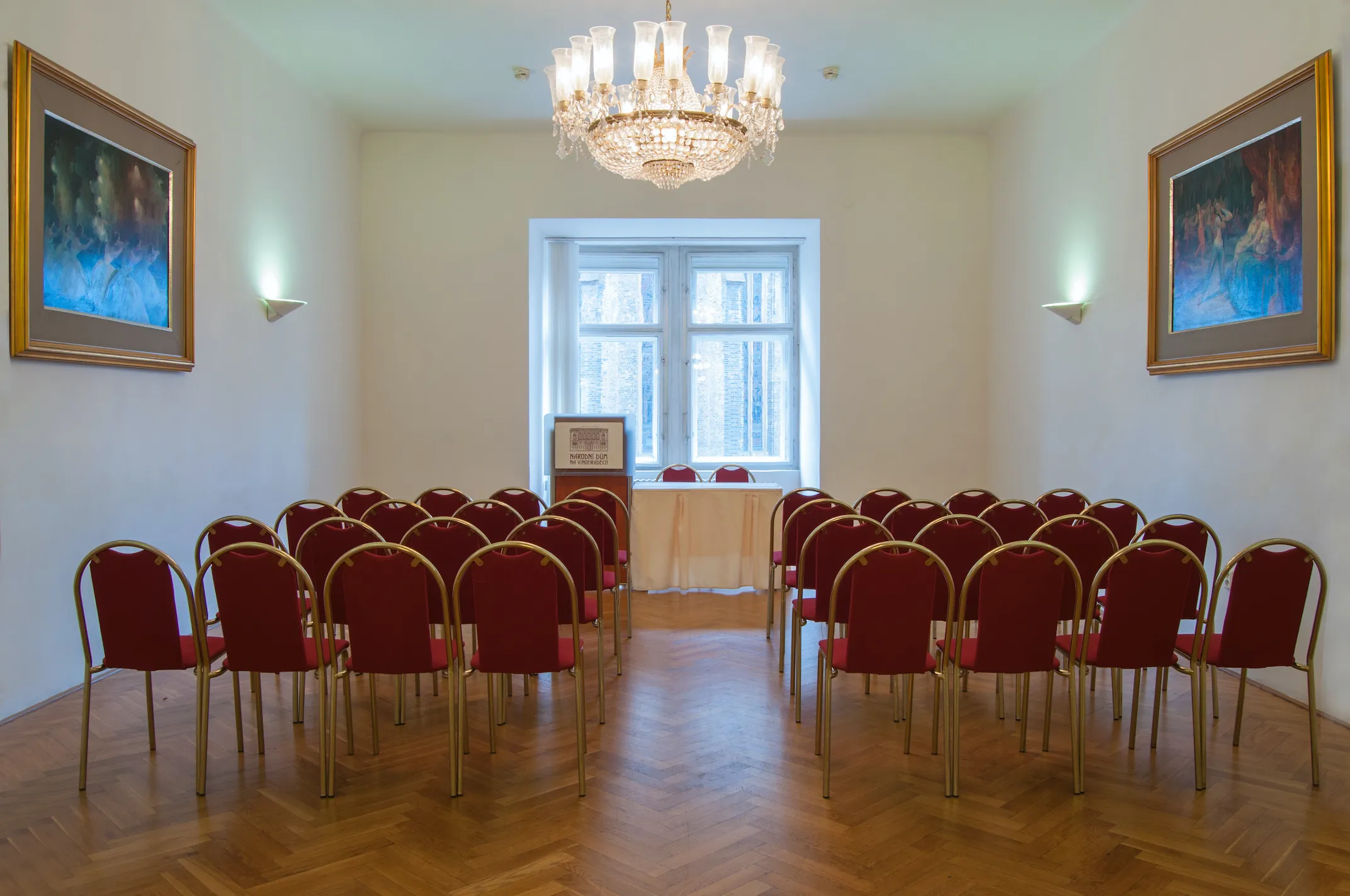 Rows of red chairs in a hall with a chandelier and framed artwork
