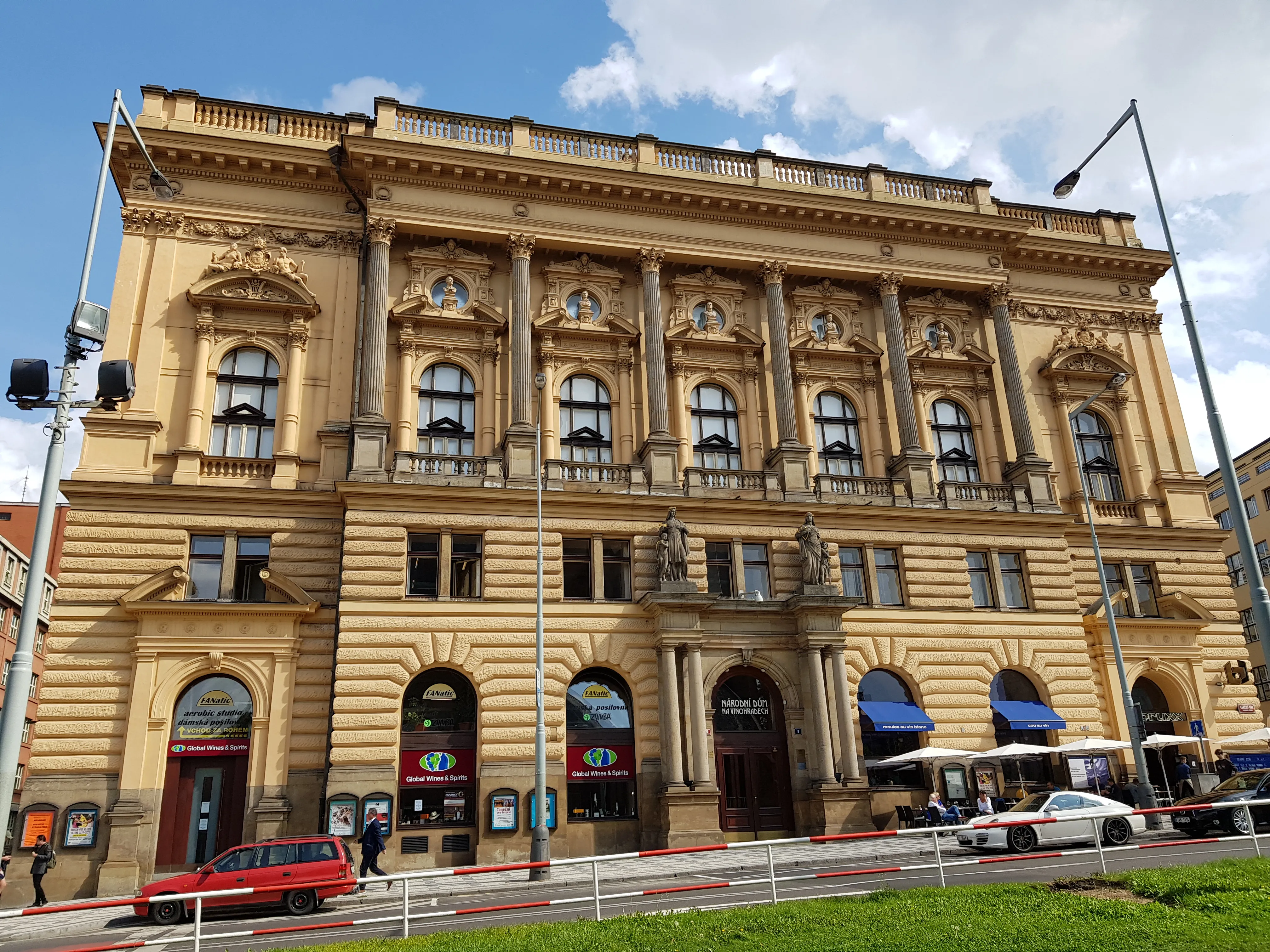 Neo-Renaissance building with ornate facade, arched windows, and blue awnings on a city street