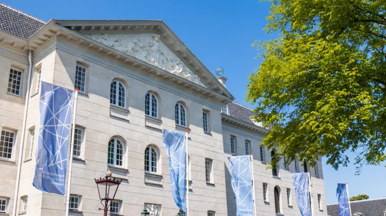 Historic stone building facade with blue banners and arched windows under a clear blue sky, part of the National Maritime Museum