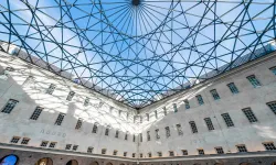 Courtyard with glass and steel roof structure, white building facade with multiple windows, and blue sky visible above
