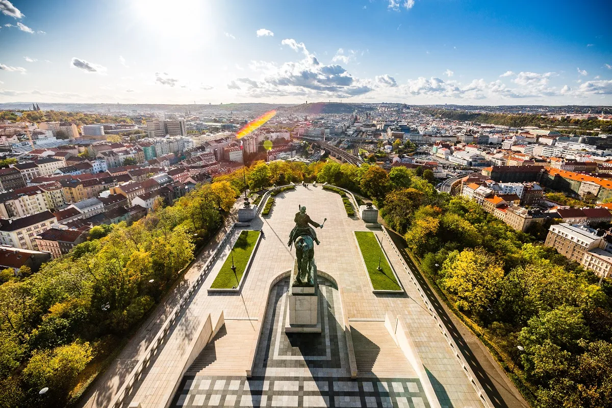 Vista aérea del Monumento Nacional en Vítkov con una gran estatua ecuestre en el centro, rodeada de árboles y un paisaje urbano bajo un cielo azul.