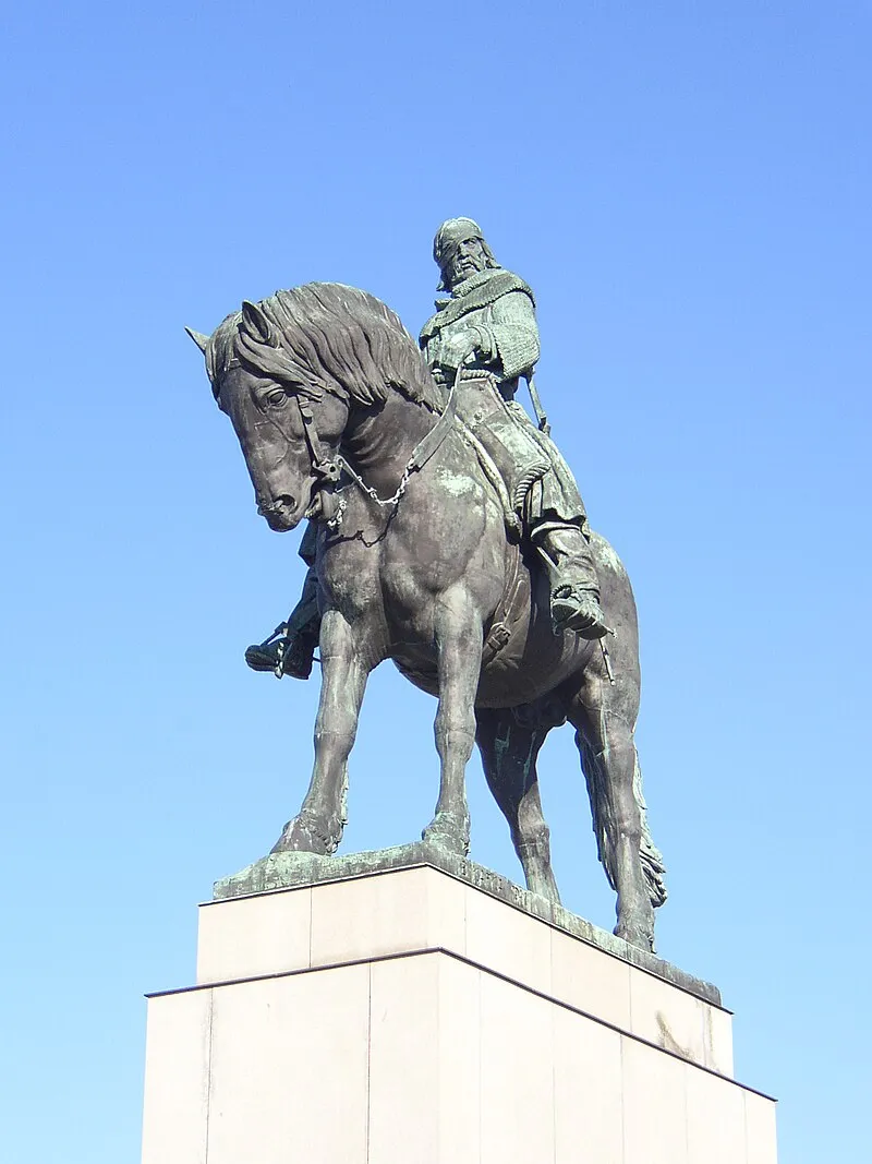 Estatua ecuestre de bronce de un hombre a caballo sobre un pedestal de piedra bajo un cielo azul