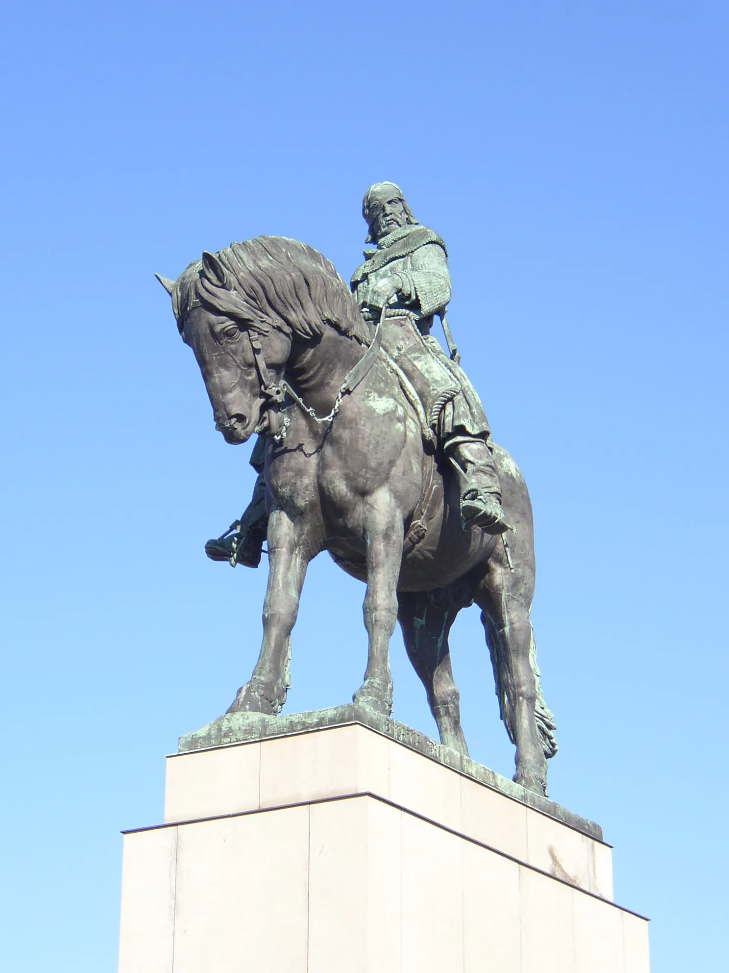 Estatua ecuestre de bronce de un hombre a caballo sobre un gran pedestal contra un cielo azul