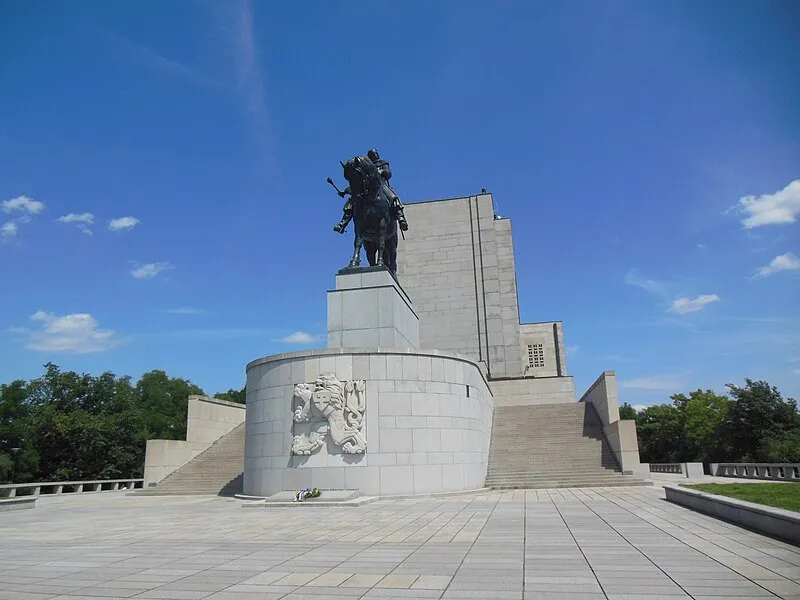 Gran estatua ecuestre sobre un pedestal de piedra con un edificio modernista detrás bajo un cielo azul