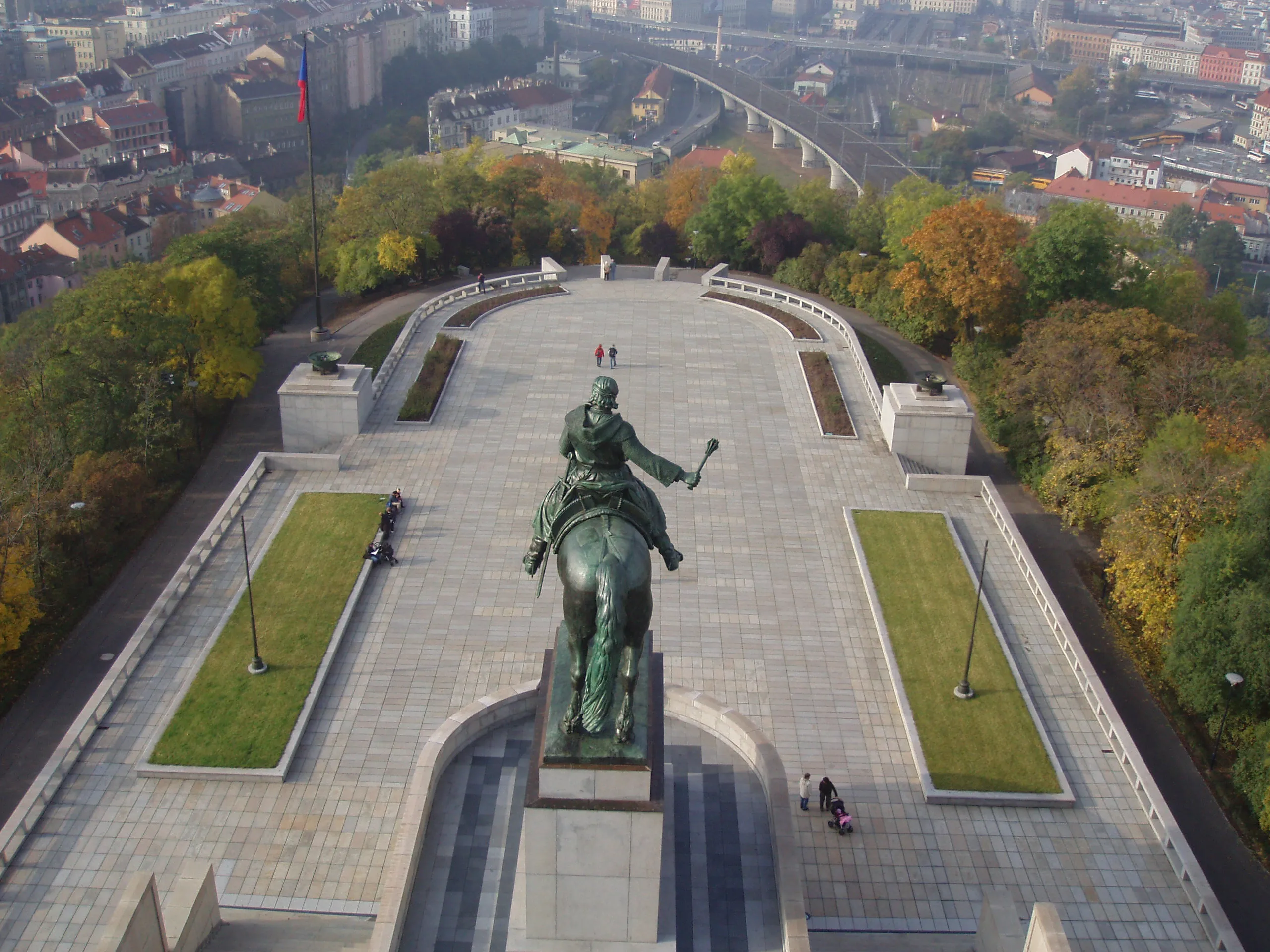 Vista aérea de una gran estatua ecuestre sobre un pedestal en una amplia plaza con un paisaje urbano al fondo