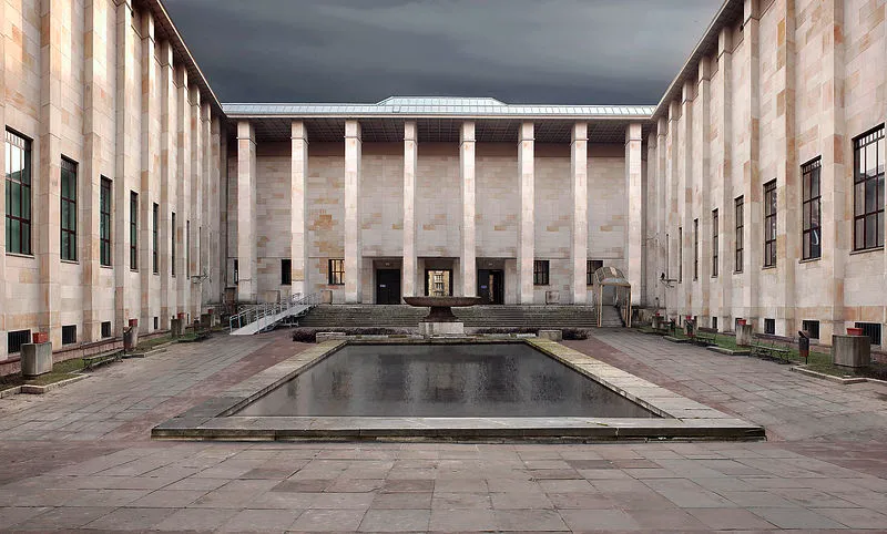 Edificio neoclásico con altas columnas y un patio central con una piscina reflectante