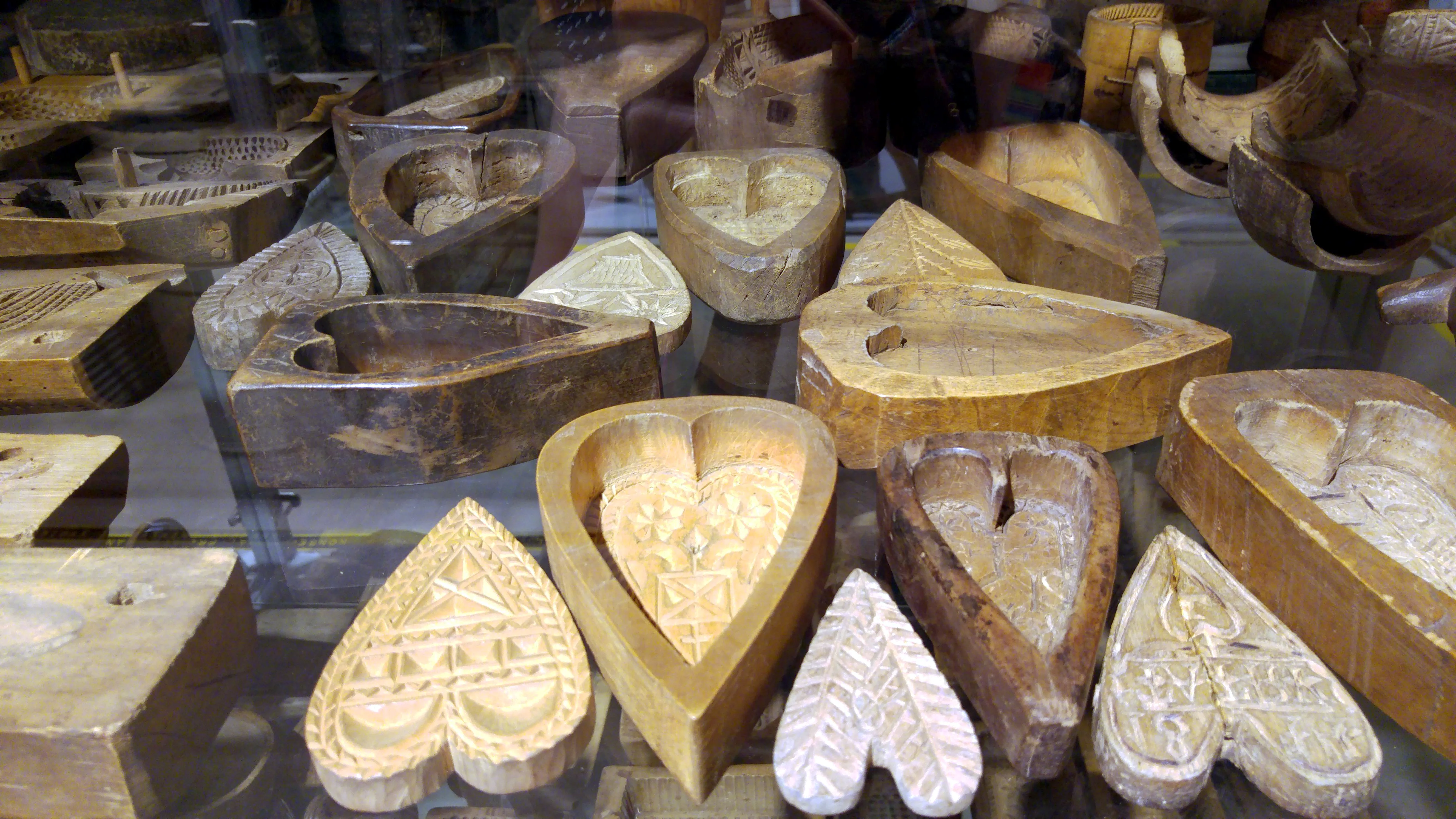 houten mallen met uitgesneden patronen, waaronder harten en boten, tentoongesteld in een glazen vitrine