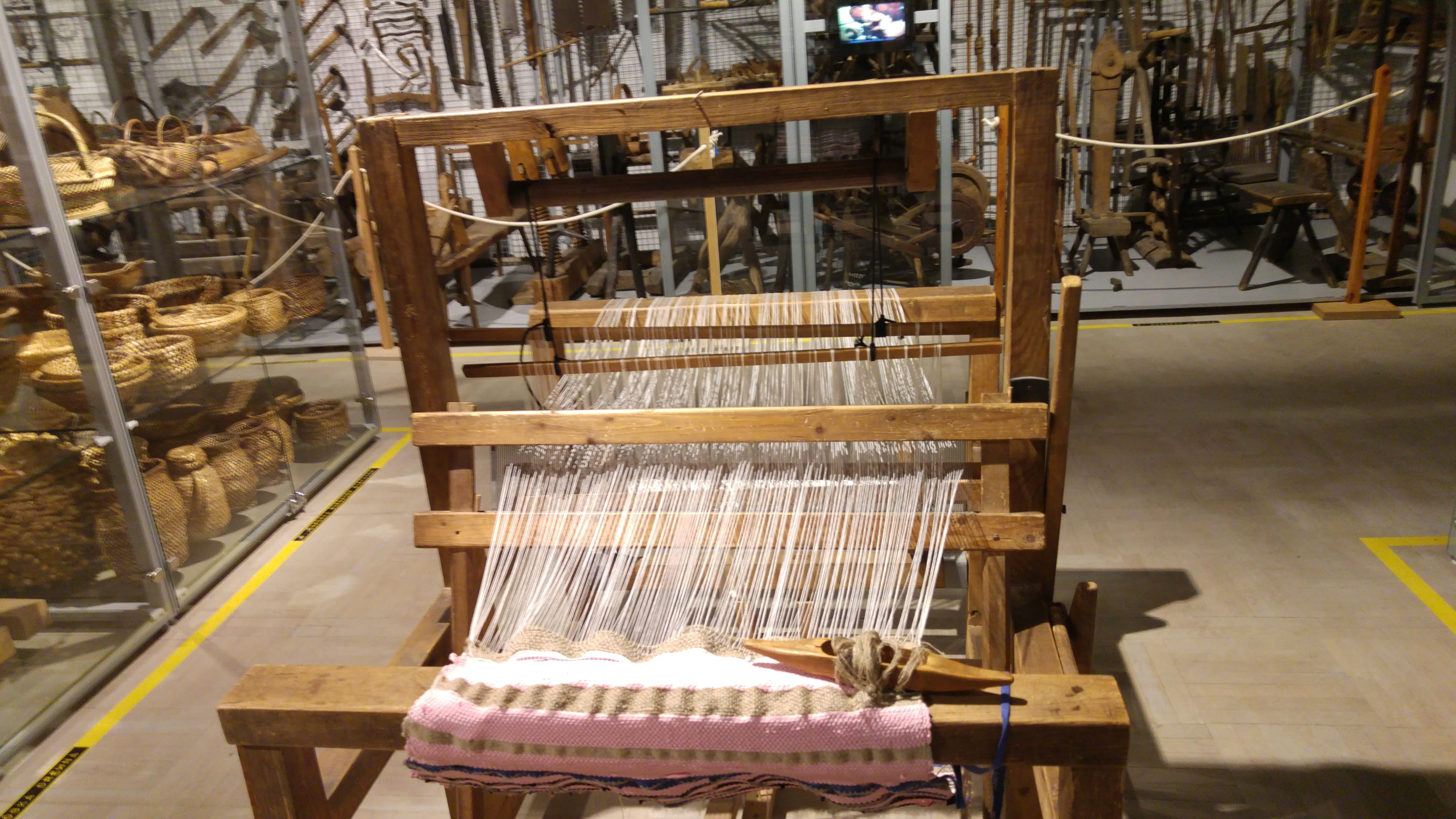 houten weefgetouw met draden en geweven stof in een museumtentoonstelling
