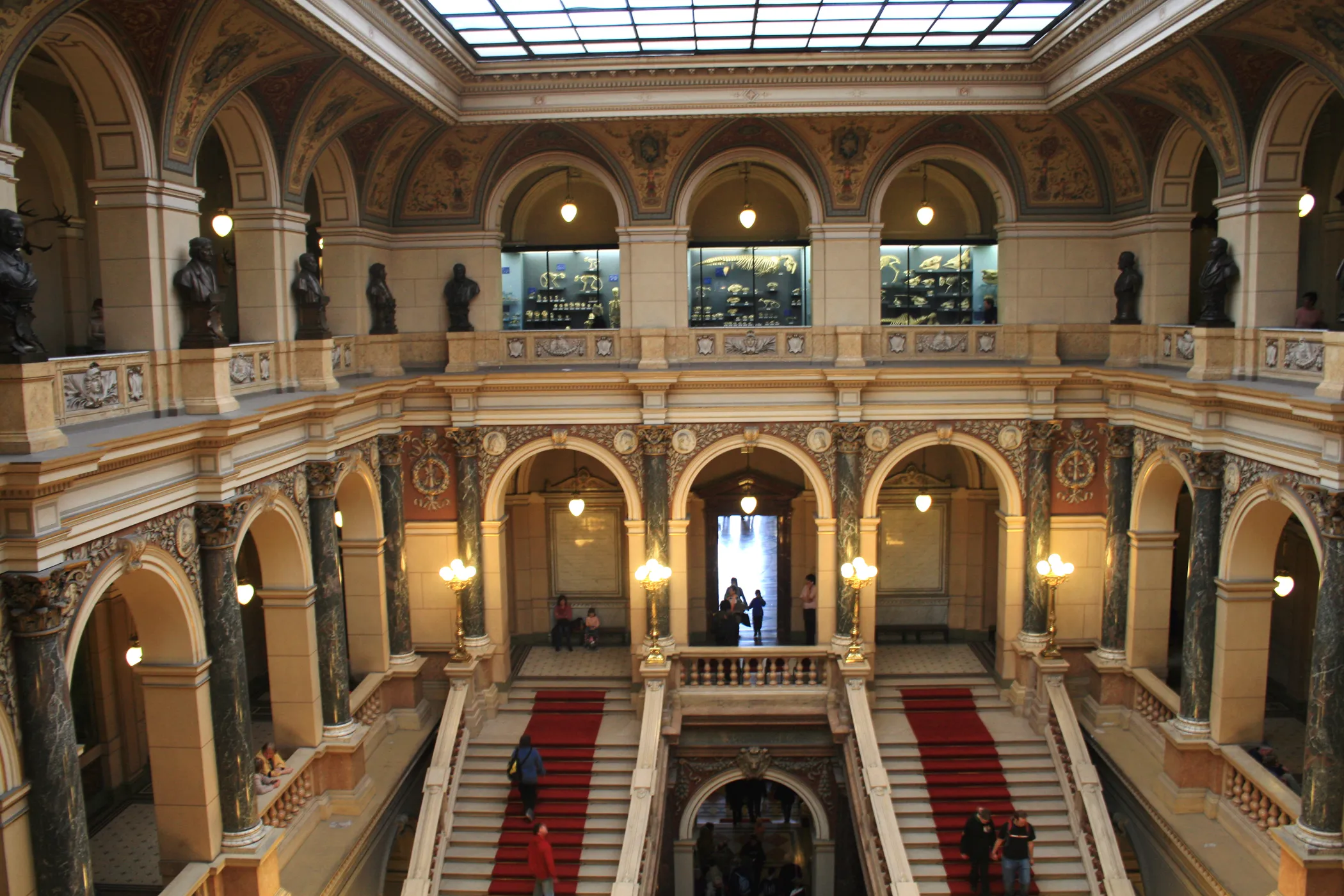 Grote inkomhal met gewelfde colonnades, een met rood tapijt beklede trap en een glazen daklicht