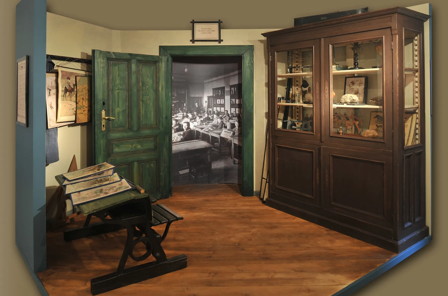 Interieur van een museumexpositie met een houten kast, een schrijftafel en een deuropening naar een andere kamer met een historische foto