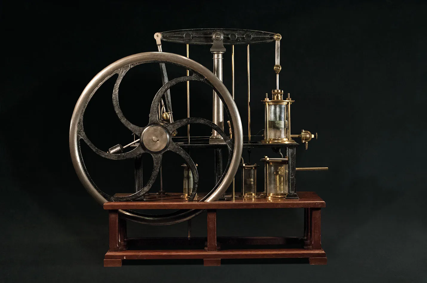Un instrumento científico vintage con una rueda grande y componentes de vidrio sobre un soporte de madera