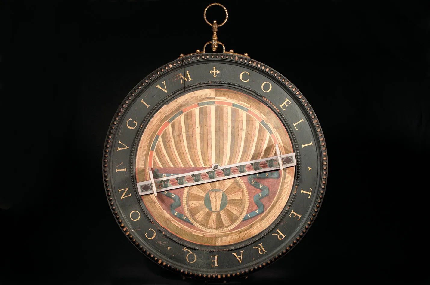Instrumento científico circular con texto en latín y motivos decorativos sobre fondo oscuro
