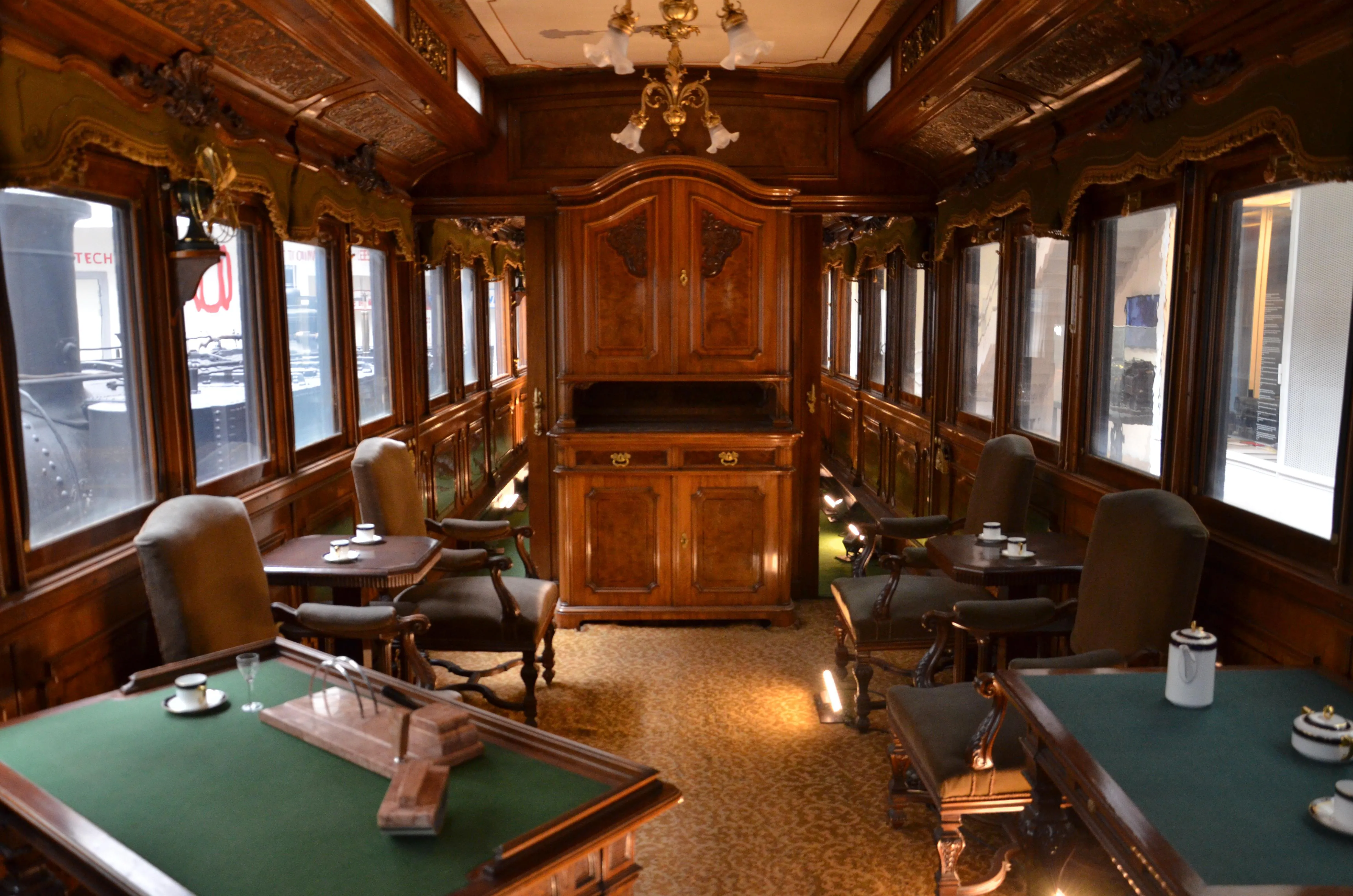 Interior of a vintage train car with wooden paneling, large windows, and green-felt tables