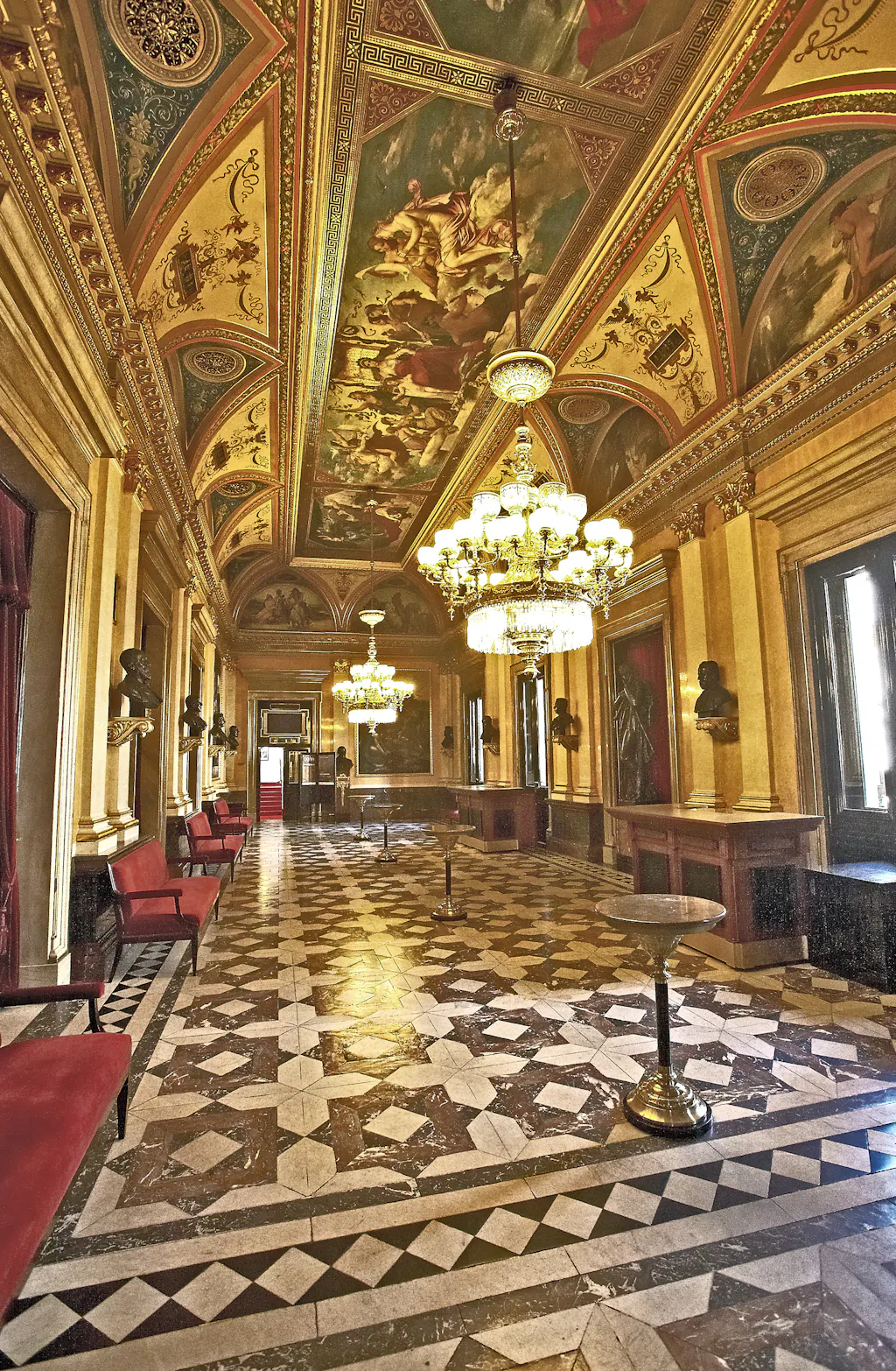 Ornate hallway with frescoed ceiling, chandeliers, and marble floor in the National Theatre