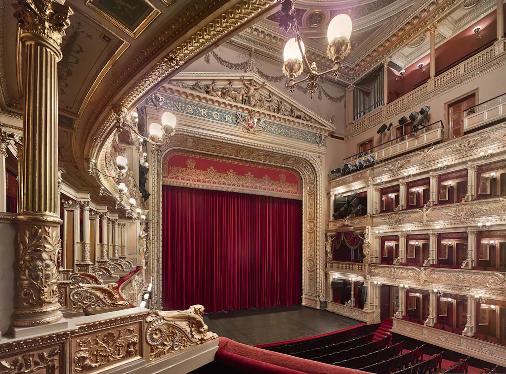 Ornate interior of the National Theatre with golden columns, red curtains, and tiered balconies